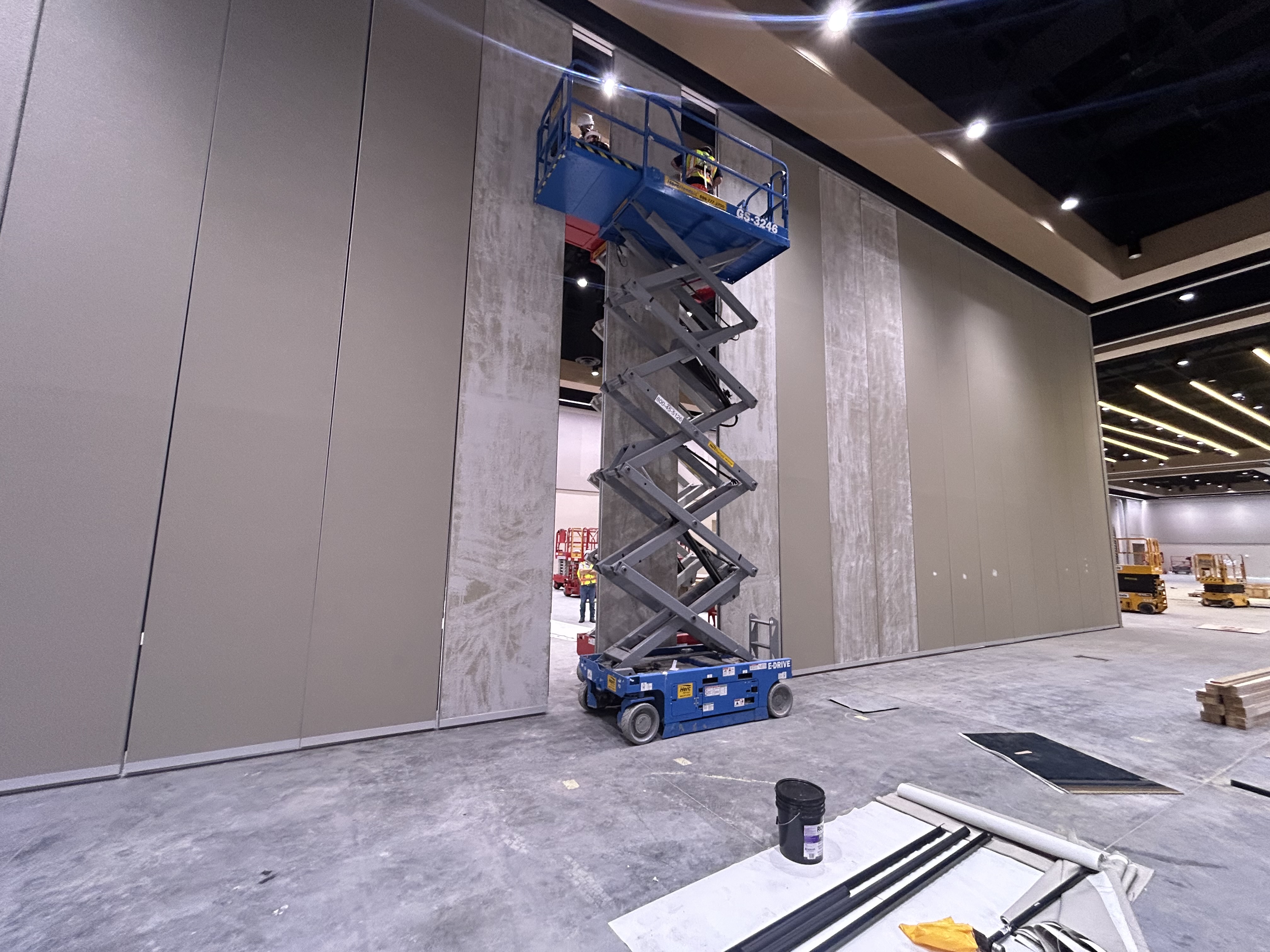 Technicians restoring tall Moderco trimless operable partition panels from a blue scissor lift.