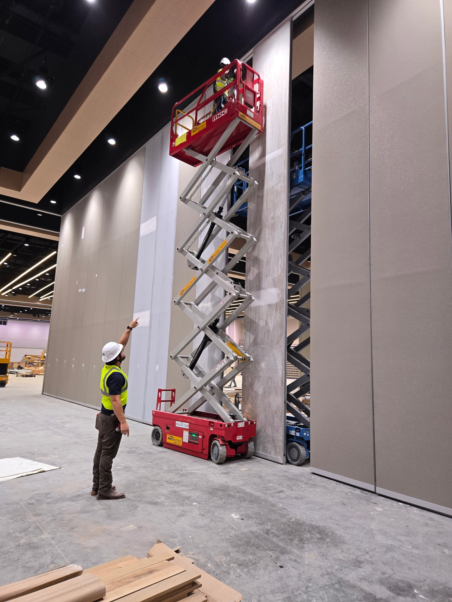 Two technicians using a scissor lift to repair a 30-foot Moderco operable partition panel.