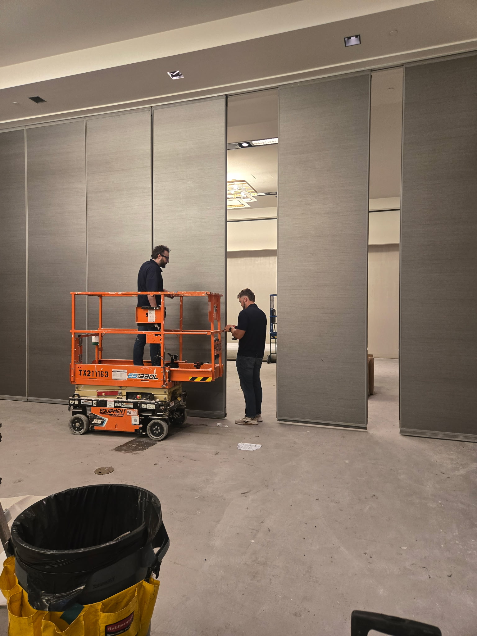 Two MotionSpan technicians working beside tall Hufcor operable partition panels with an orange lift at W Austin.