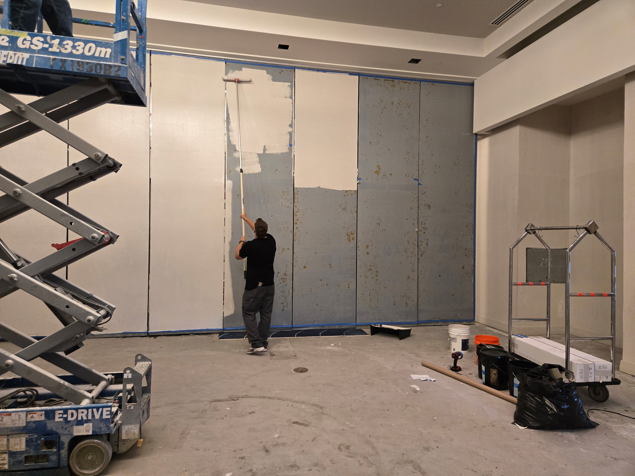 MotionSpan technician applying rust-inhibiting primer to Hufcor operable partition panels with a roller at W Austin.